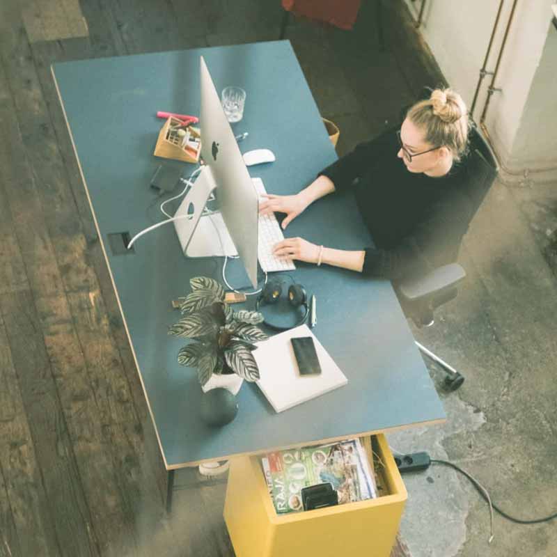 Moderner Schreibtisch im Coworking Space mit Frau vor dem Computer